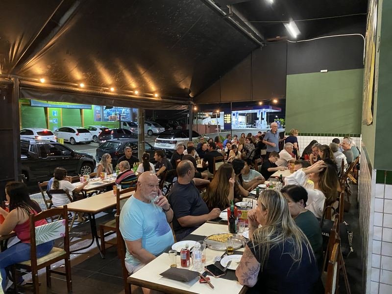 Mesas na calçada do Bar do Ari com clientes sob o varal de luzes
