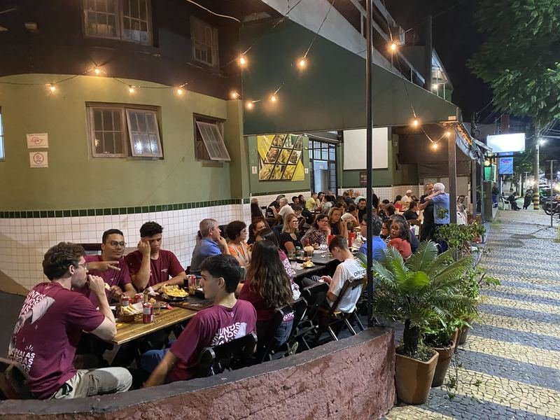 Salão coberto do Bar do Ari com mesas ocupadas à noite